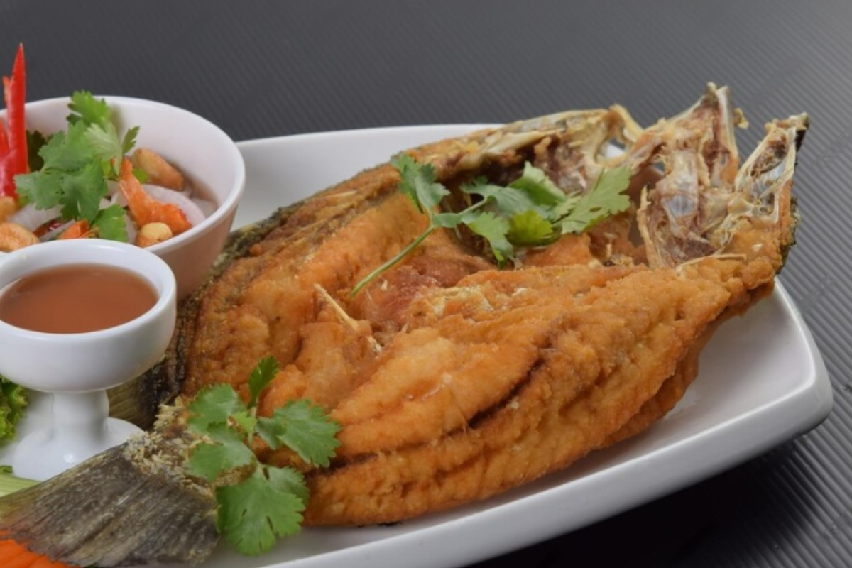 A crispy, golden-brown Fried Daing na Bangus on a plate, served with a side of vinegar dipping sauce. The marinated bangus belly is perfectly fried, with a crunchy texture and a deliciously flaky inside. 