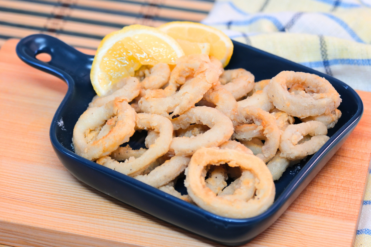 A plate of crispy golden calamari rings, freshly fried and served with a side of lemon wedges.