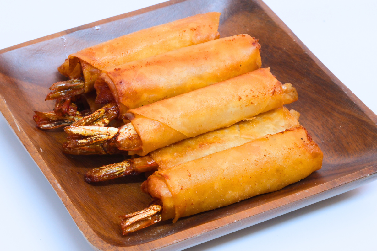 Golden-brown Crispy Shrimp Spring Rolls on a wooden plate.