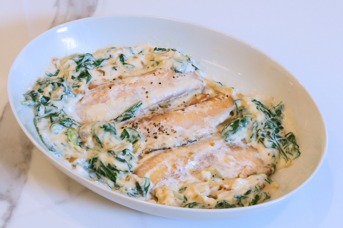 A bowl of Ginataang Tilapia, featuring golden fried Fishta Tilapia fillets simmered in a creamy coconut milk sauce with spinach, garlic, and ginger.