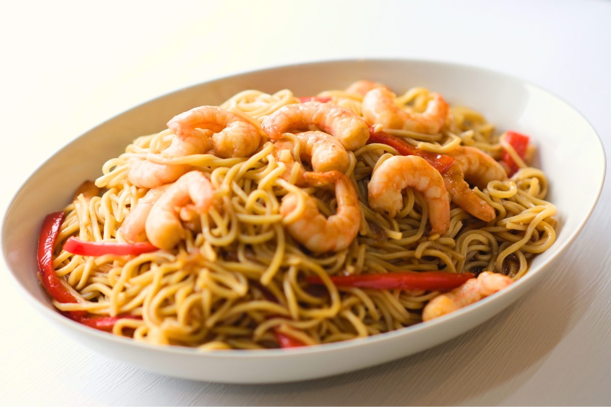 A plate of Long Life Noodles with Shrimp, featuring golden egg noodles tossed in a flavorful sauce with fresh Fishta Shrimp, bell peppers, and onions.