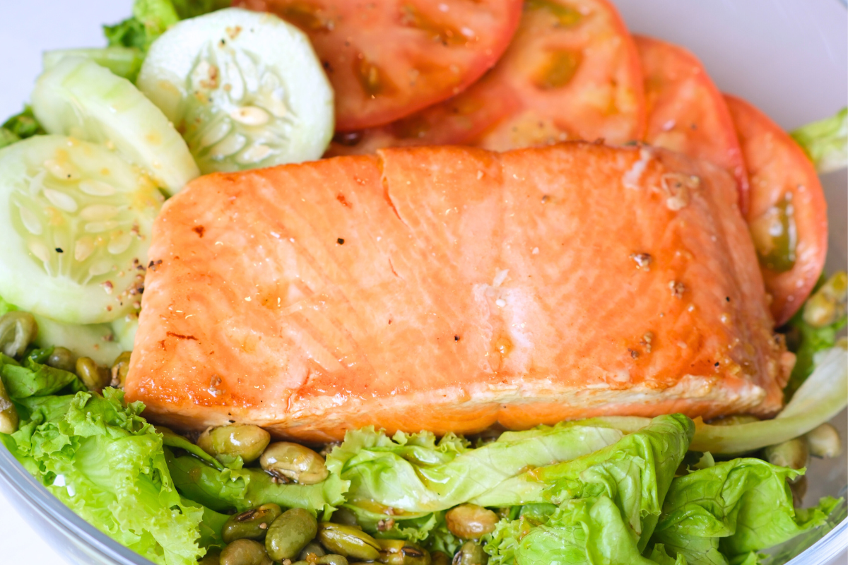 A fresh Salmon Salad topped with grilled salmon, cherry tomatoes, cucumbers, and edamame, drizzled with a rich ginger sesame dressing.